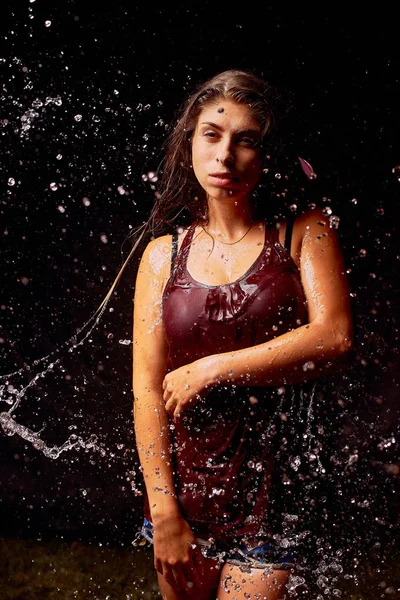 Splashes of water on the young woman on dark background