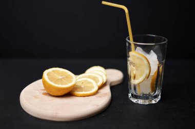 Tahtada dilimlenmiş limon meyvesi, buz küpleri ve bardakta samanla.