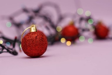 Pembe arka planda çelenk renkli ışıklar ile kırmızı noel topları
