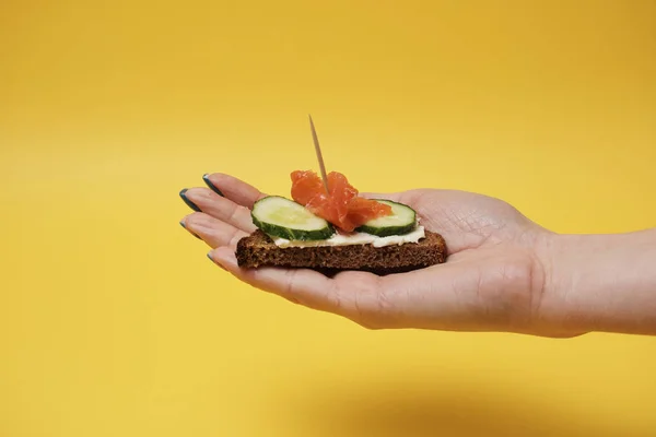 Mujer Sosteniendo Sándwich Salmón Mano Sobre Fondo Amarillo — Foto de Stock