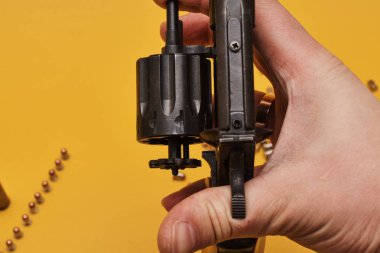 Sarı arka planda tabanca tutan kişinin kısmi görüntüsü