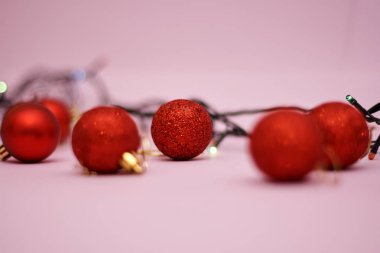 Pembe arka planda çelenk renkli ışıklar ile kırmızı noel topları