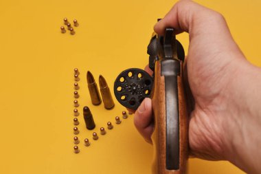 Erkek elinde silah ve sarı arka planda kurşunlar.