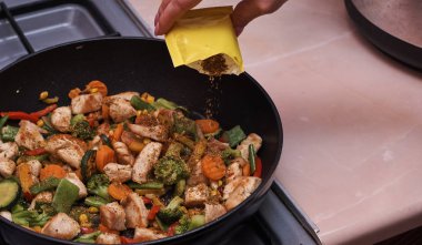 Kadın tavuk etiyle karışık sebze pişiriyor.