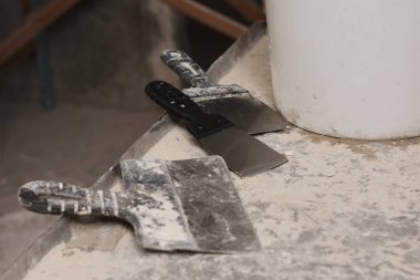 Beton bir yüzey duvarında beyaz kovayla paslı aletler.