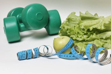 Beyaz arka plan, diyet kavramı izole mavi ölçüm bandı ve dambıl ile marul yaprağı ve elma.