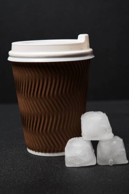 Siyah arka planda tek kullanımlık kahve fincanı ve buz küplerinin yakın plan görüntüsü