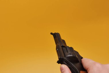 Sarı arka planda insan elinin tabancayı tutuşu kısmi görünüm