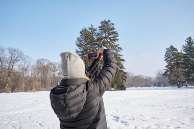 Genç bir kadının cep telefonuyla muhteşem kış manzarasının fotoğrafını çektiği arka plan görüntüsü.