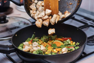 Kadın tavuk etiyle karışık sebze pişiriyor.