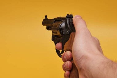İnsan elinin sarı arka planda tabancayı tutarken kısmi görüntüsü