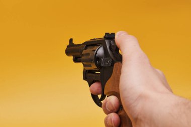 Sarı arka planda insan elinin tabancayı tutuşu kısmi görünüm
