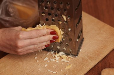 Kadının rendelenmiş peyniri rendeleyen kısmi görüntüsü.