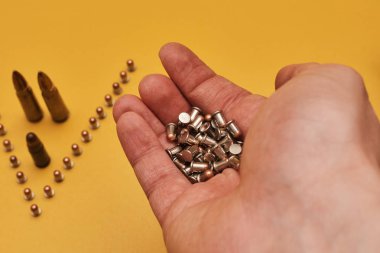 Sarı arka planda kurşunları tutan kişinin kısmi görüntüsü 