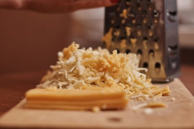 Kadının rendelenmiş peyniri rendeleyen kısmi görüntüsü.