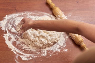 Ahşap bir tahtanın üzerinde hamur yoğuran bir kadın resmi.  