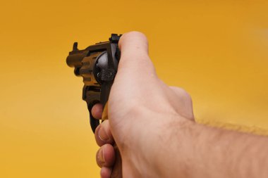 İnsan elinin sarı arka planda tabancayı tutarken kısmi görüntüsü