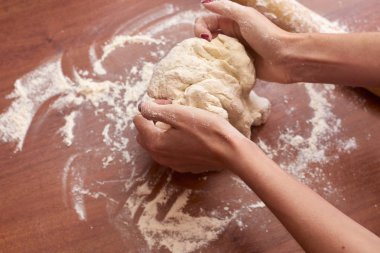 Ahşap bir tahtanın üzerinde hamur yoğuran kadının ellerini kapat.  