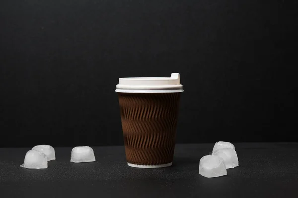 close-up view of disposable coffee cup and ice cubes on black background