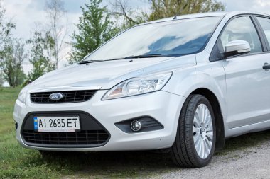 Bulutlu bir günde kırsal yolda park edilmiş gümüş rengi parlak bir araba.       