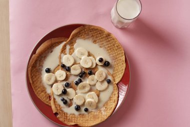 Siyah üzümlü krep ve bir bardak sütle servis edilen muz.