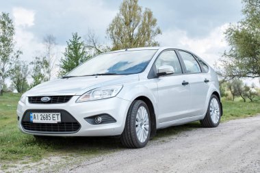 Bulutlu bir günde kırsal yolda park edilmiş gümüş rengi parlak bir araba.     