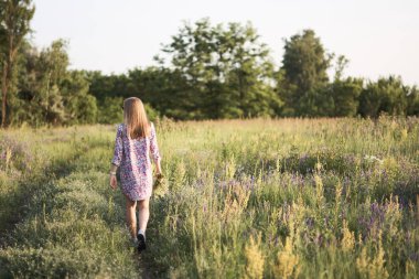 Çiçeklerle tarlada poz veren genç ve güzel bir kadın.