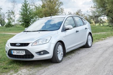 Bulutlu bir günde kırsal yolda park edilmiş gümüş rengi parlak bir araba.    