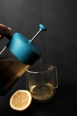 Elinde çaydanlık olan ve bardağa çay döken birinin kırpılmış görüntüsü. 