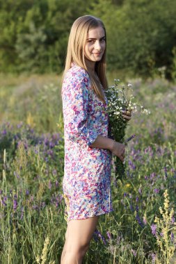 Çiçeklerle tarlada poz veren genç ve güzel bir kadın.