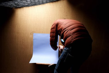 Ahşap duvarın yanında boş mavi kağıtla yerde çömelmiş bir adam. 