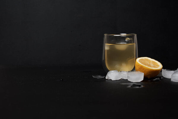 glass of lemonade with lemon and ice cubes on dark background 