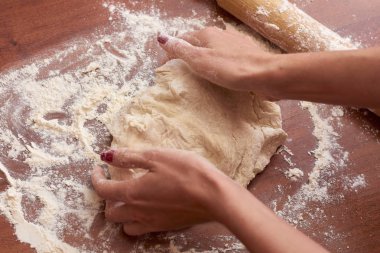 Ahşap bir tahtanın üzerinde hamur yoğuran kadının ellerini kapat.  