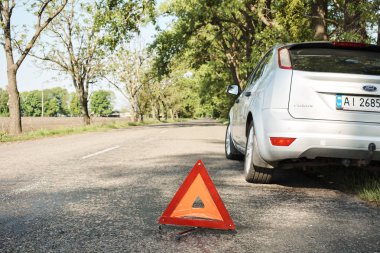 Kırık arabayı uyarmak için yolda bulunan kırmızı üçgen sembol. Yolda duran acil durum arabası, bozuk araba konsepti..   