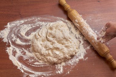 Ahşap bir tahtanın üzerinde hamur yoğuran bir kadın resmi.  