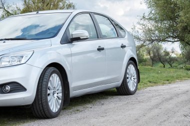 Bulutlu bir günde kırsal yolda park edilmiş gümüş rengi parlak bir araba. 