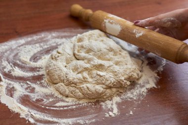 Ahşap bir tahtanın üzerinde hamur yoğuran bir kadının eli. 