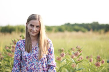 Çiçeklerle tarlada poz veren genç ve güzel bir kadın.