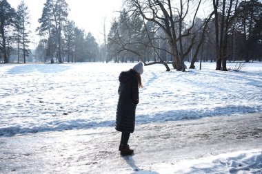 Sarışın kadın karlı kış parkında yürüyor.