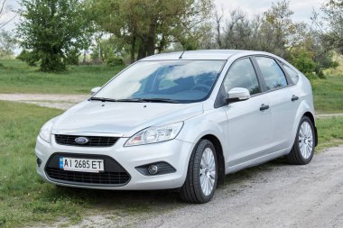 Bulutlu bir günde kırsal yolda park edilmiş gümüş rengi parlak bir araba.     