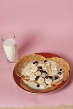 Siyah üzümlü krep ve bir bardak sütle servis edilen muz.