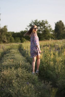 Çiçeklerle tarlada poz veren, elbiseli ve güneş gözlüklü güzel bir kadın.