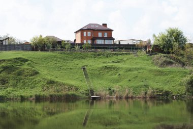 Yansıtıcı göl manzarası ve yeşil tepedeki evler 