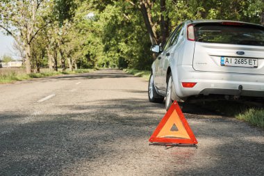 Kırık arabayı uyarmak için yolda bulunan kırmızı üçgen sembol. Yolda duran acil durum arabası, bozuk araba konsepti..    