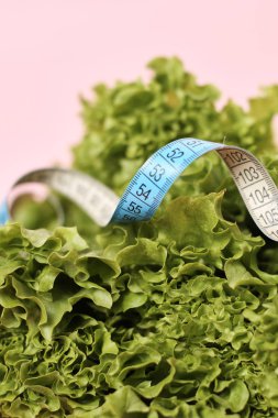 Ölçüm bandı, diyet kavramı ile pembe arka plan üzerinde taze salata yaprakları.