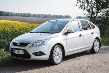 Bulutlu bir günde kırsal yolda park edilmiş gümüş rengi parlak bir araba.   