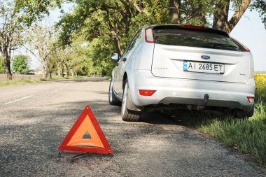 Kırık arabayı uyarmak için yolda bulunan kırmızı üçgen sembol. Yolda duran acil durum arabası, bozuk araba konsepti..  