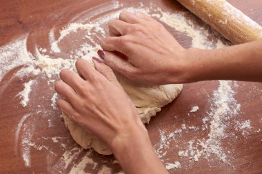 Ahşap bir tahtanın üzerinde hamur yoğuran kadının ellerini kapat.  