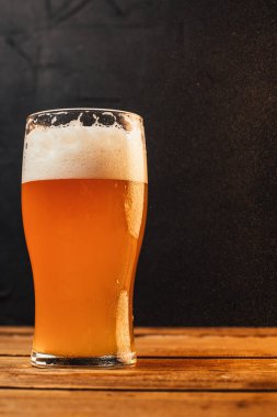 Siyah arka planda, ahşap masada, cam içinde soğuk biranın yakın plan görüntüsü. 