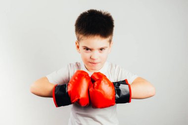 Boks eldivenli ciddi bir çocuk gri arka planda kameraya bakıyor.